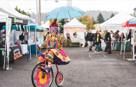 female clown in colorful skirt on bike holding an umbrella