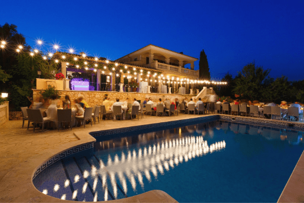 Private event with dinner tables and string lights by the pool